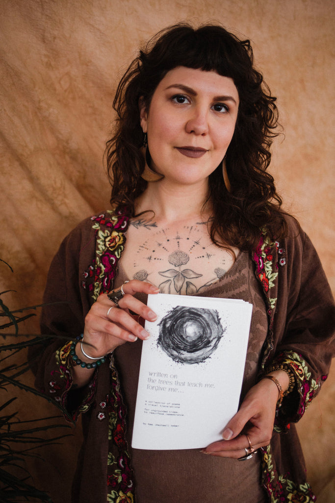 Rachael Amber smiles holding her cyclical poetry book "written on the trees that teach me, forgive me..."